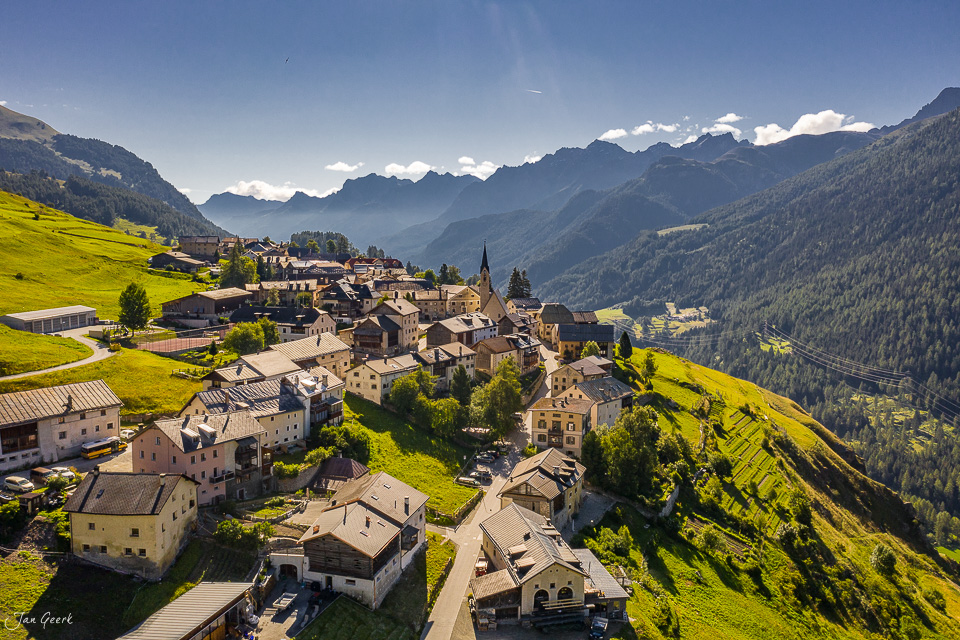Luftaufnahme des historischen Dorfes Guarda mit Kirche, grünen Hängen und Bergkulisse im Sommer – Graubünden Schweiz – Jan Geerk Fotograf Basel