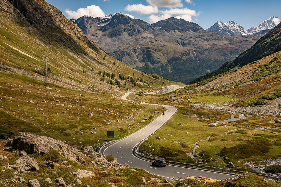 Kurvenreiche Passstrasse durch grüne Alpweiden mit schneebedeckten Bergen im Hintergrund am Julierpass Graubünden Schweiz – Jan Geerk Fotograf Basel