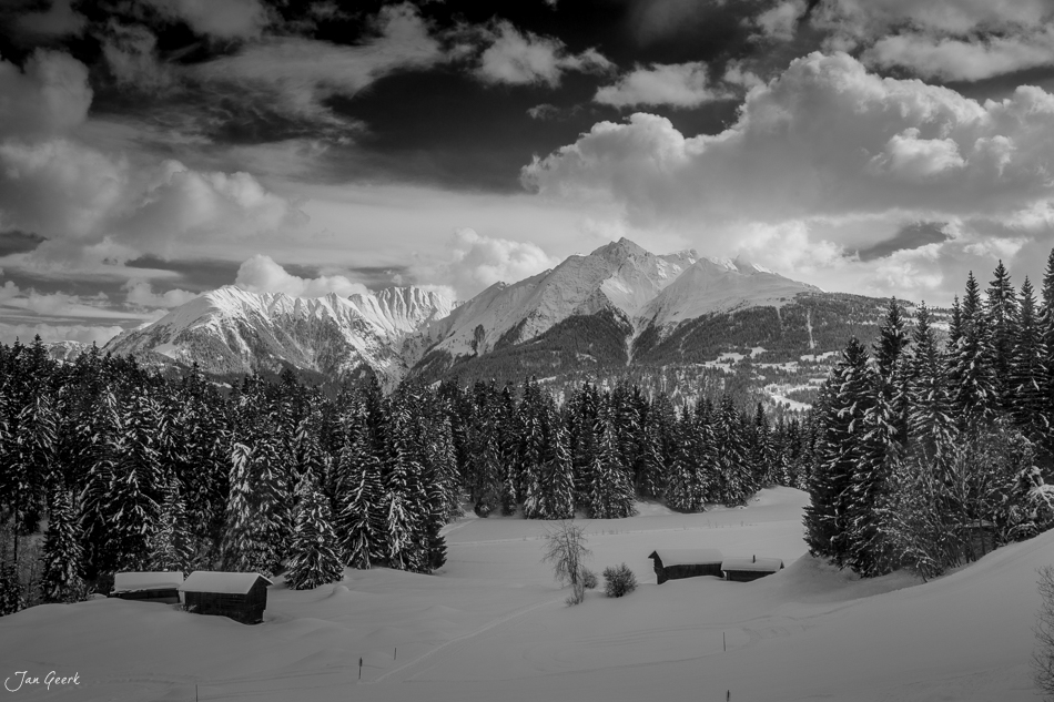 Schneebedeckte Berglandschaft mit Berghütten Lärchenwäldern und schneebedeckten Bergen bei Laax, Graubünden, Schweiz – Jan Geerk Fotograf Basel
