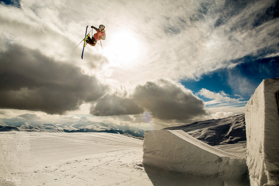 Snowboarder in der Halfpipe von Laax springt hoch in die Luft mit schneebedeckten Bergen und dramatischem Himmel – Schweiz Jan Geerk Fotograf Basel