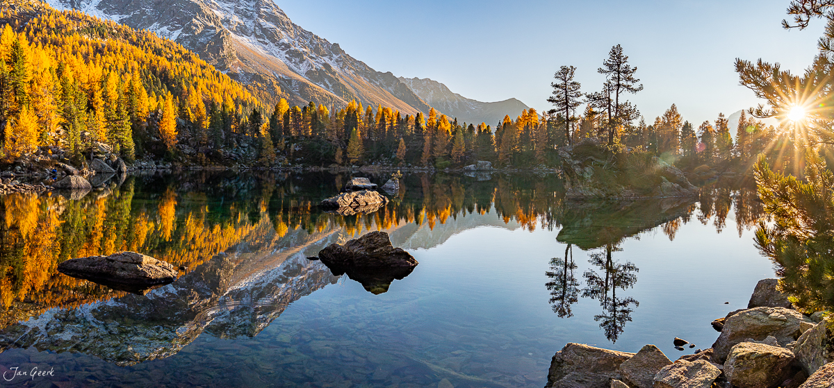 Spiegelglatter Bergsee mit goldenem Lärchenwald, verschneiter Bergspitze, Herbststimmung Graubünden Schweiz – Jan Geerk Fotograf Basel
