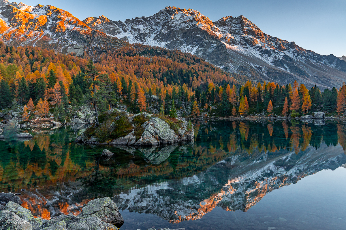 Herbstliche Lärchenwald-Spiegelung im Lago di Saoseo mit schneebedeckten Bergen, Kantlicht Oktober, Graubünden Schweiz – Jan Geerk Fotograf Basel
