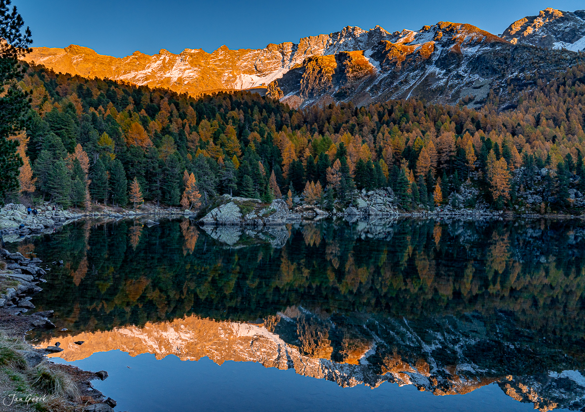 Spiegelglatter Lago di Saoseo im Herbst, umgeben von Lärchenwäldern in goldener Kantlichtstimmung, Graubünden Schweiz – Jan Geerk Fotograf Basel