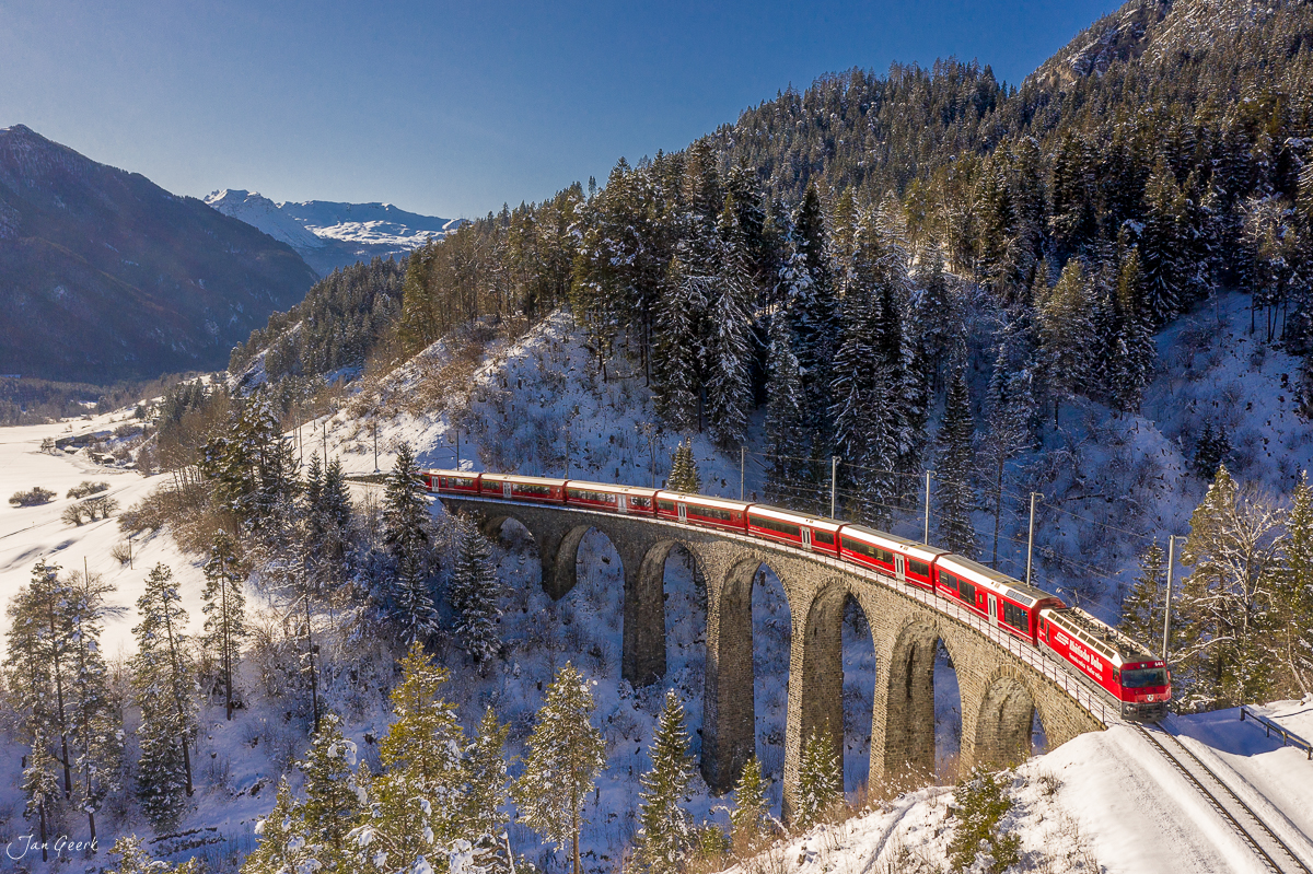 Roter Zug auf dem Landwasserviadukt mit schneebedecktem Wald und Bergpanorama im Winter in Graubünden Schweiz – Jan Geerk Fotograf Basel