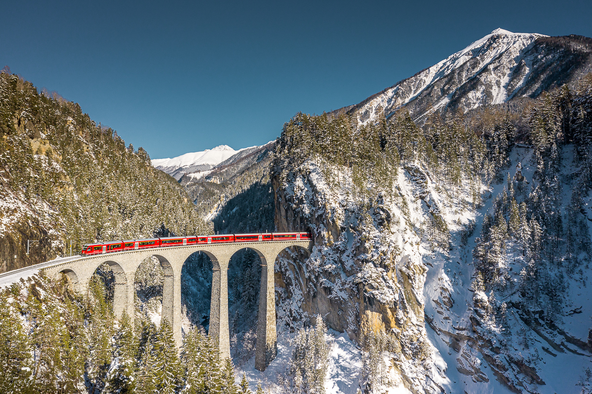 Landwasserviadukt Filisur mit rotem Zug im Winter, schneebedeckte Berge, Graubünden Schweiz – Jan Geerk Fotograf Basel