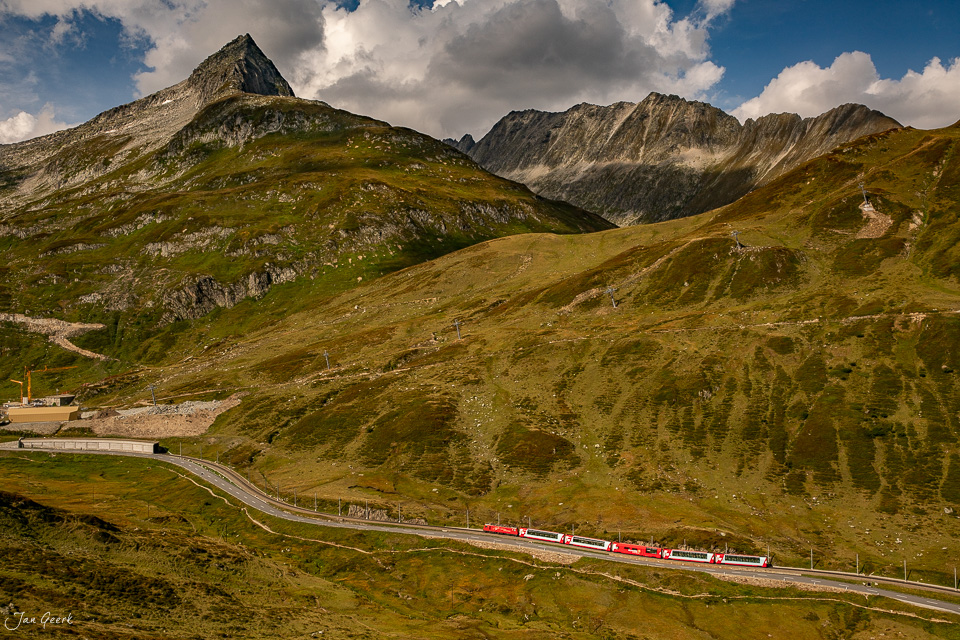 Roter Zug auf Bergbahn am Oberalppass mit grünen Alpweiden und markanten Gipfeln in Graubünden Schweiz – Jan Geerk Fotograf Basel