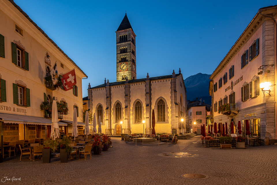 Beleuchtete Kirche mit Glockenturm auf dem Dorfplatz in Poschiavo bei Nacht, Graubünden Schweiz – Jan Geerk Fotograf Basel