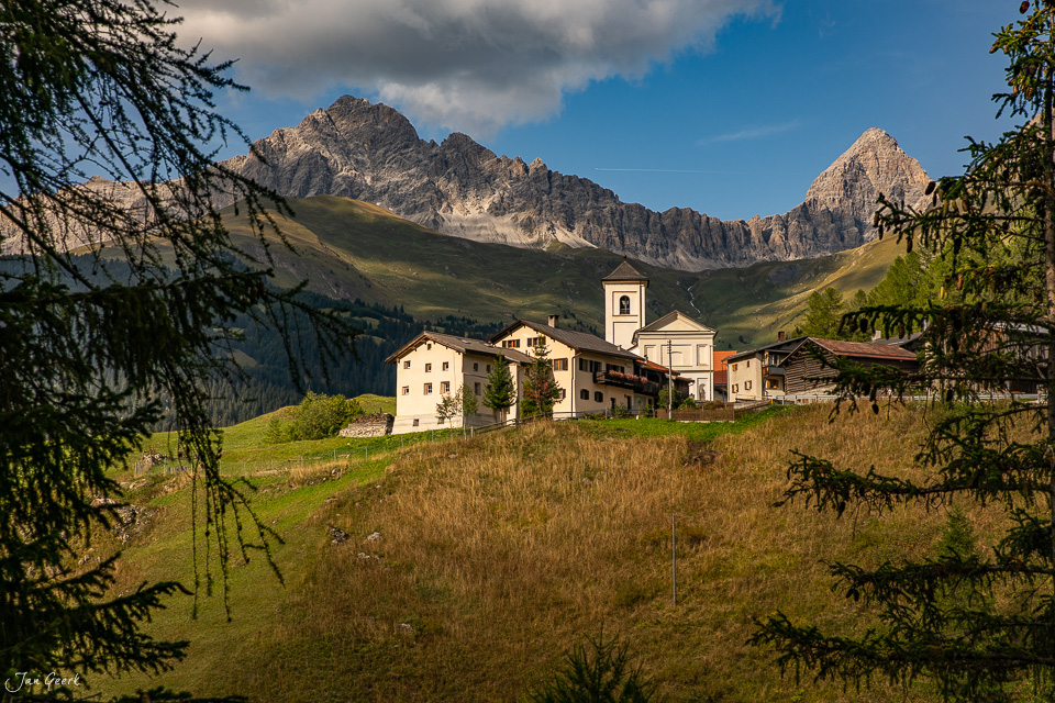 Dorf Rona mit Kirche und Bergen im Hintergrund, Sommerliche Alplandschaft, Graubünden Schweiz – Jan Geerk Fotograf Basel