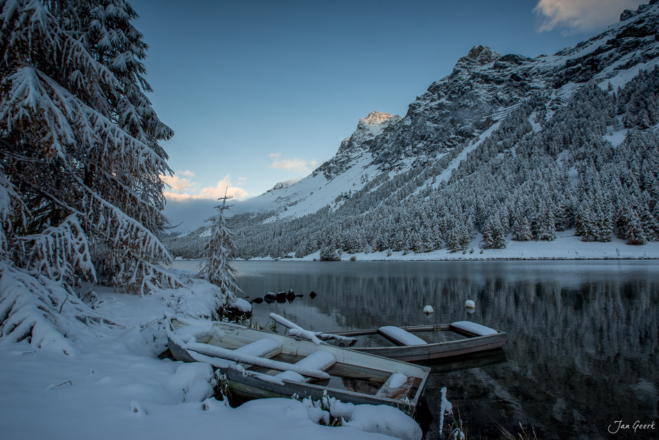 Verschneite Boote am Silsersee mit winterlichen Lärchenwäldern und Bergen im Engadin Graubünden Schweiz – Jan Geerk Fotograf Basel