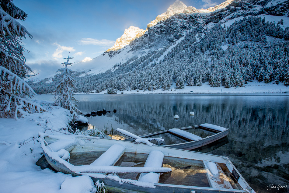 Verschneite Ruderboote am Silsersee im Winter mit schneebedeckten Bergen und Wald, Engadin Graubünden Schweiz – Jan Geerk Fotograf Basel