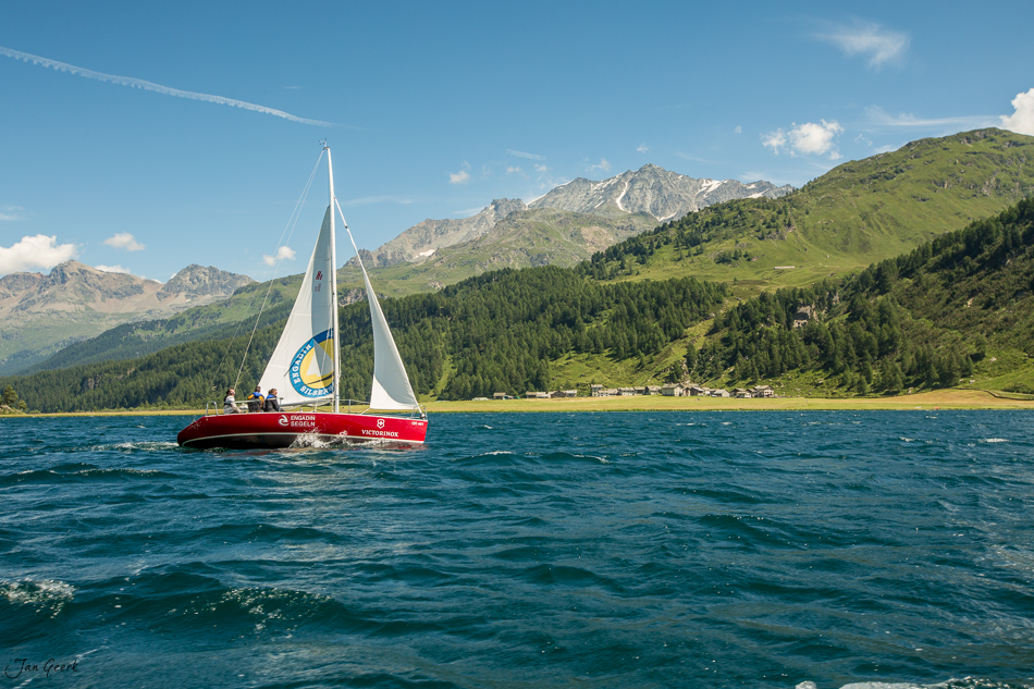 Rotes Segelboot mit weißem Segel auf dem Silsersee, umgeben von grünen Bergen und Wäldern, Sommertime in Graubünden Schweiz – Jan Geerk Fotograf Basel
