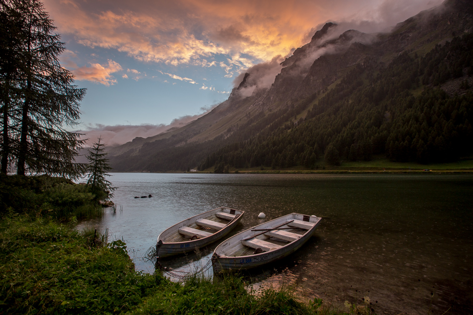 Zwei Holzboote am Ufer des Silsersee mit majestätischen Bergen im goldenen Sommerlicht, Engadin Graubünden Schweiz – Jan Geerk Fotograf Basel