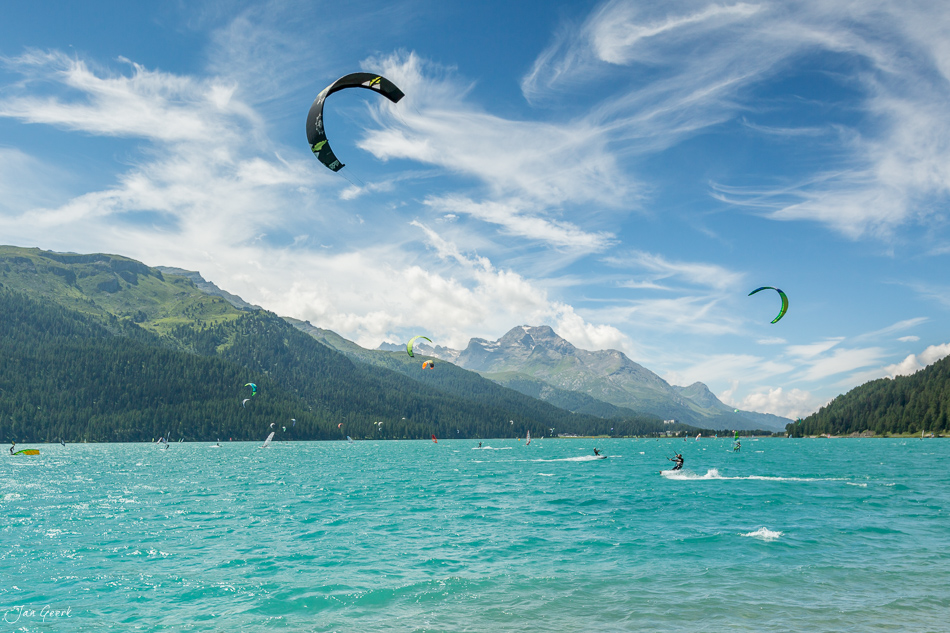 Kitesurfer und Segelboote auf dem türkisblauen Wasser des Silvaplana mit schneebedeckten Berggipfeln und Bergwald im Engadin Graubünden Schweiz – Jan Geerk Fotograf Basel