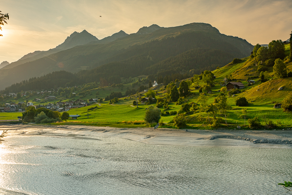 Alpendorf Brigels an der Surselva mit grünen Wiesen, Bergen und Fluss in Sommerlicht Graubünden Schweiz – Jan Geerk Fotograf Basel