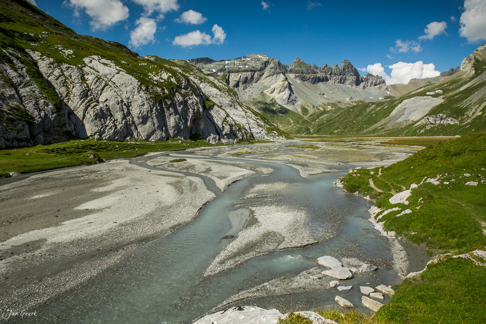 Gletschermilchfluss Segnesboden mit Alpenmassiv, grüne Wiesen, blauer Himmel, Sommer Graubünden Schweiz – Jan Geerk Fotograf Basel