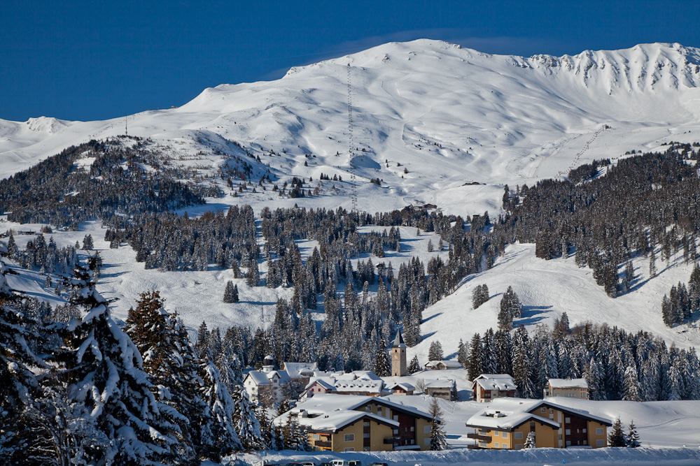 Schneebedeckte Berglandschaft mit Bergdorf Kirche Nadelwald Winter Graubünden Schweiz – Jan Geerk Fotograf Basel