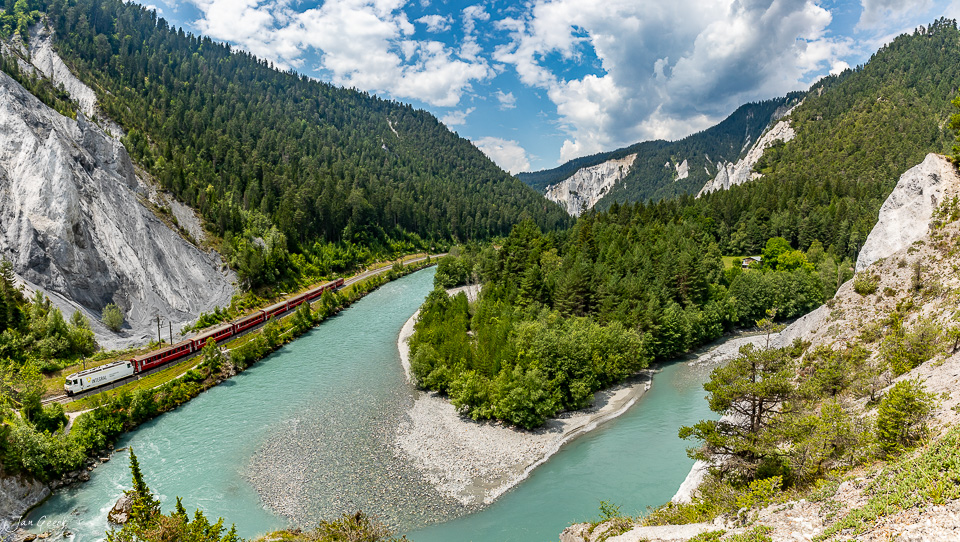 Zug mit rotem Waggon fährt durch die Rheinschlucht neben türkisem Fluss zwischen Felswänden und Nadelwald Graubünden Schweiz Jan Geerk Fotograf Basel