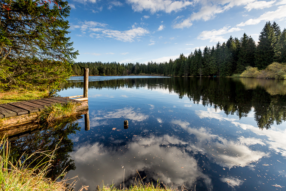 Stiller Bergsee im Jura mit Holzsteg, Herbstlicht und Nadelwaldreflexion Schweiz – Jan Geerk Fotograf Basel