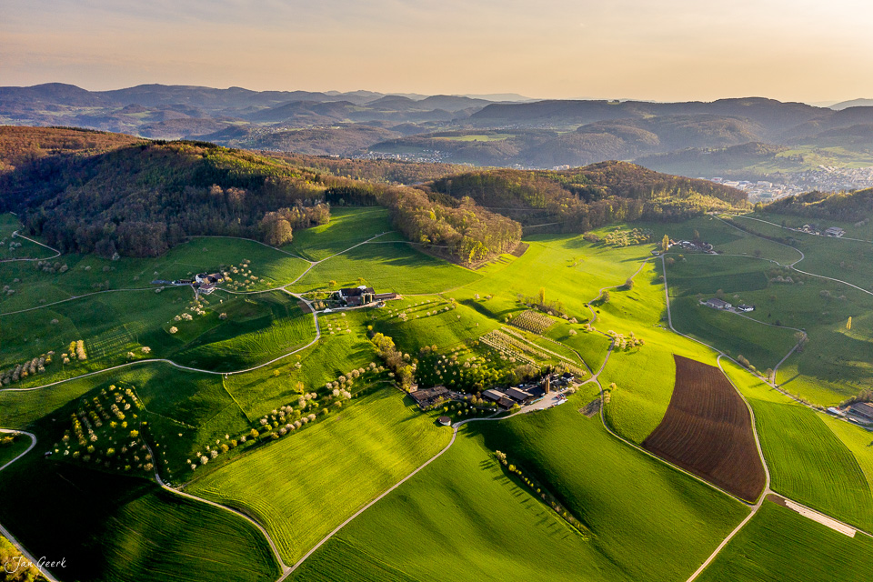 Luftaufnahme der Frühlings-Kulturlandschaft bei Arisdorf mit grünen Feldern, Bauernhöfen und Wäldern in Baselland, Schweiz – Jan Geerk Fotograf Basel
