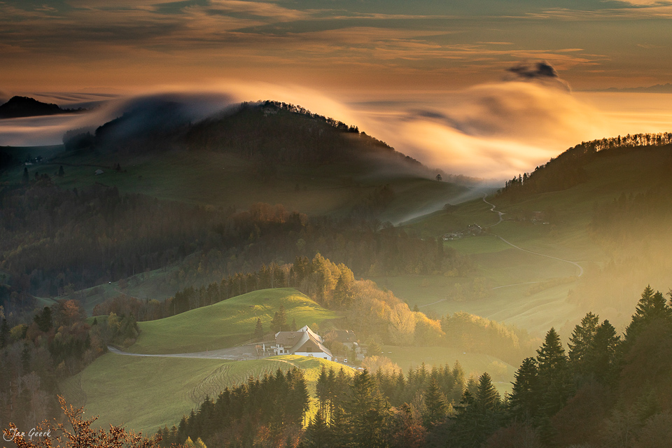 Herbstliche Berglandschaft mit Nebel über bewaldeten Hügeln und traditionellem Bauernhaus im Tal, Bölchen Nordwestschweiz – Jan Geerk Fotograf Basel