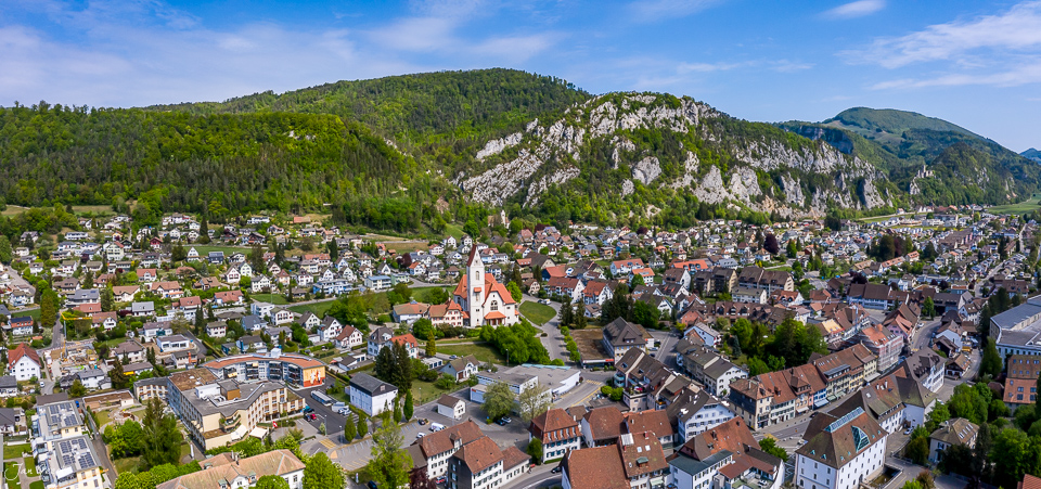 Luftaufnahme Dorf Balsthal mit Kirche, Häusern und bewaldeten Bergen im Frühling, Solothurn Schweiz – Jan Geerk Fotograf Basel
