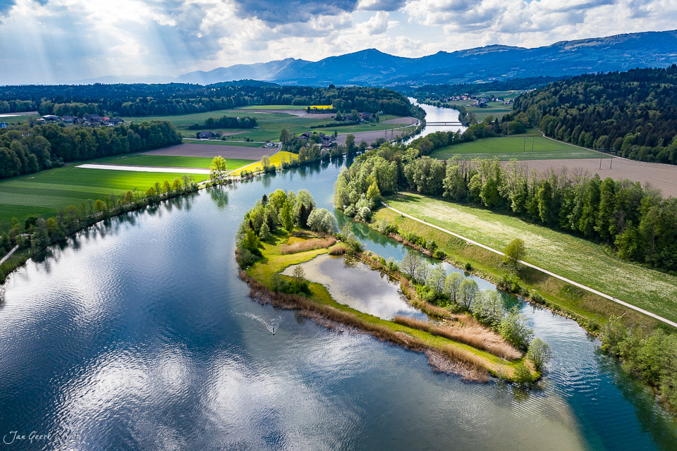 Luftaufnahme der Aare bei Bannwil mit grünen Wiesen, Wäldern und Bergen im Hintergrund, sonnige Frühjahrsstimmung im Mittelland Schweiz – Jan Geerk Fotograf Basel