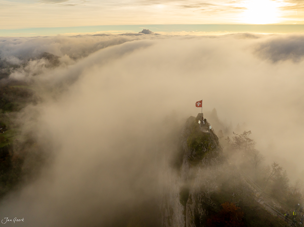 Schweizer Flagge auf Felsengipfel über Nebelwelle Herbst Baselland Schweiz Jan Geerk Fotograf Basel