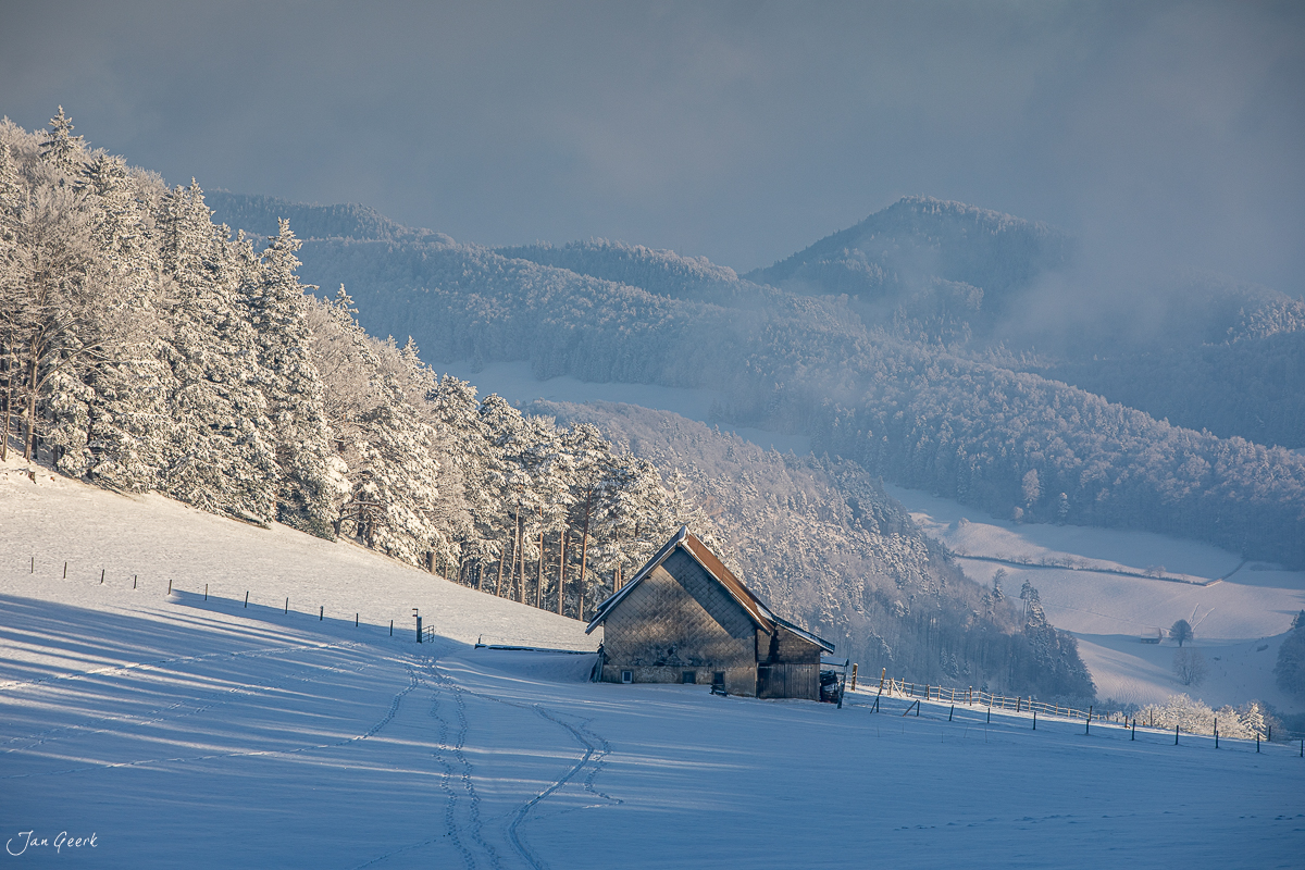 Winterlandschaft Waldweid mit schneebedeckter Scheune, gefrorener Weide und Bergpanorama bei Kantlicht Nordwestschweiz Schweiz Jan Geerk Fotograf Basel
