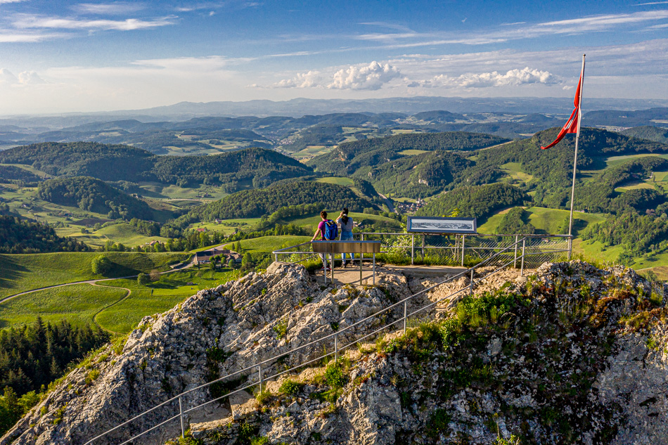 Aussichtsplattform auf dem Belchen mit Schweizer Flagge, Frühjahrsblick über grüne Hügel und Täler des Basellands, Schweiz – Jan Geerk Fotograf Basel