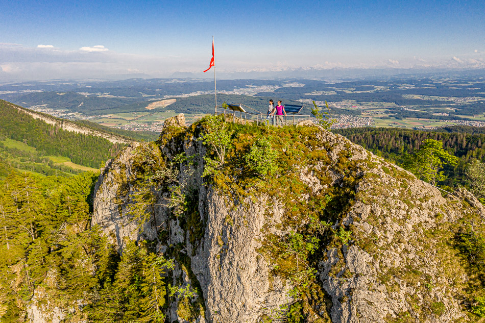 Felsformation mit Schweizer Flagge auf dem Belchen, grünes Baselbiet im Frühling, Luftaufnahme – Jan Geerk Fotograf Basel