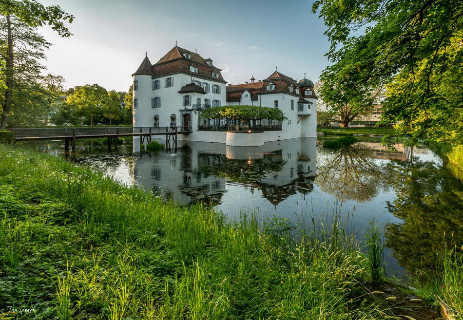 Wasserschloss Bottmingen spiegelt sich im Teich, umrahmt von grünem Laub, Frühlingsstimmung in Basel-Landschaft Schweiz – Jan Geerk Fotograf Basel