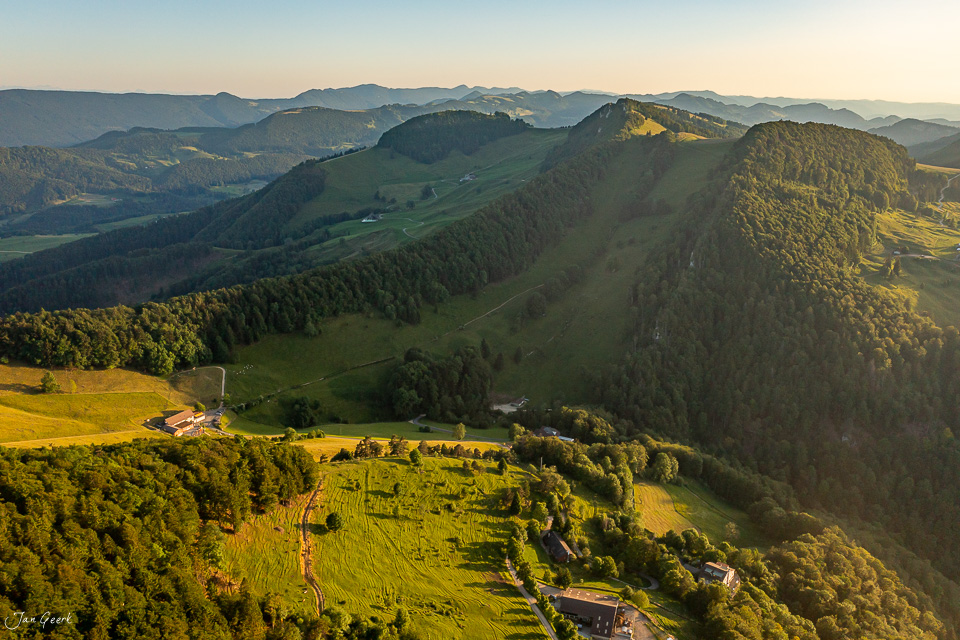 Luftaufnahme Chellechöpfli mit grünen Hügeln, Wäldern und Bauernhöfen in goldenem Sommerlicht, Baselland Schweiz – Jan Geerk Fotograf Basel