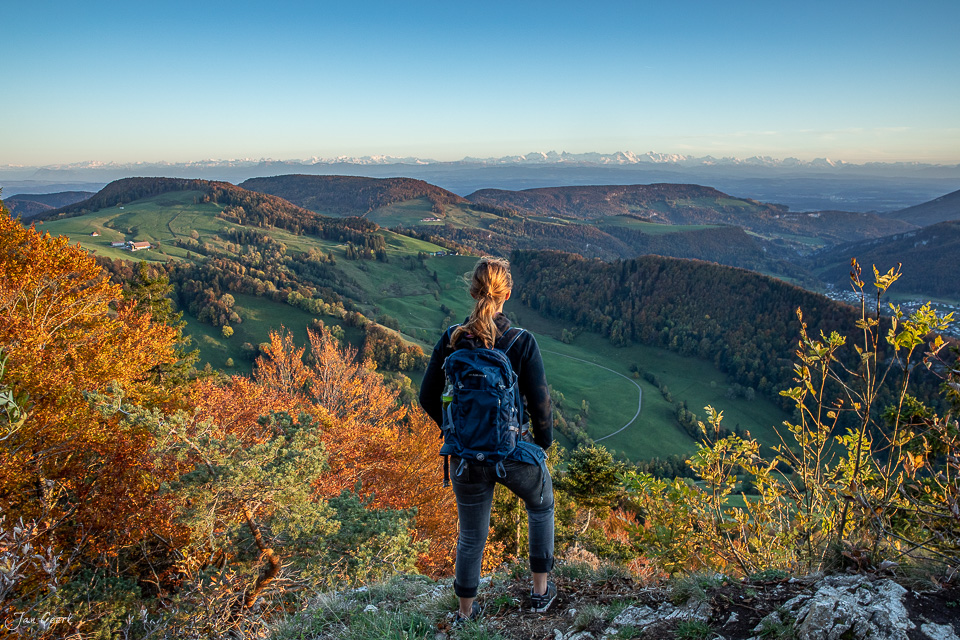 Wanderin auf Chellechöpfli blickt auf herbstliche Jura-Landschaft mit schneebedeckten Alpen im Hintergrund, Baselland Schweiz – Jan Geerk Fotograf Basel