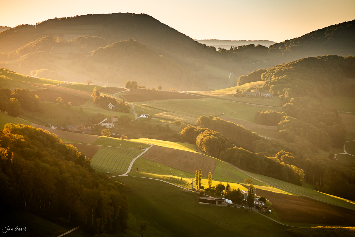 Malerische Hügellandschaft Gislifluh mit golden beleuchteten Feldern, Bauernhöfen und Waldstreifen im Morgenlicht, Aargau Schweiz – Jan Geerk Fotograf Basel