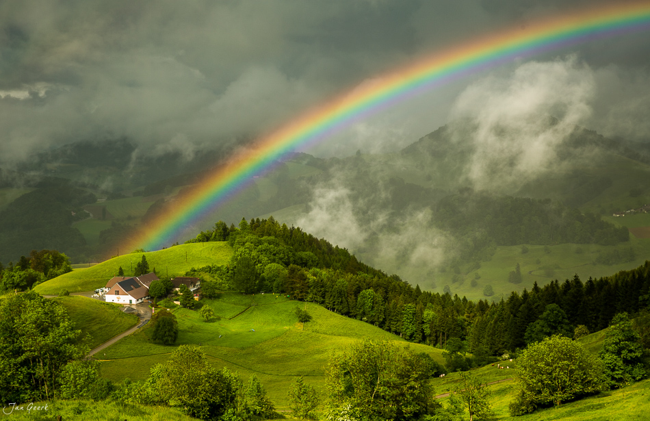 Regenbogen über grünen Hügeln und Bauernhaus in der Bölchenregion während Gewitter im Frühling, Baselland Schweiz – Jan Geerk Fotograf Basel