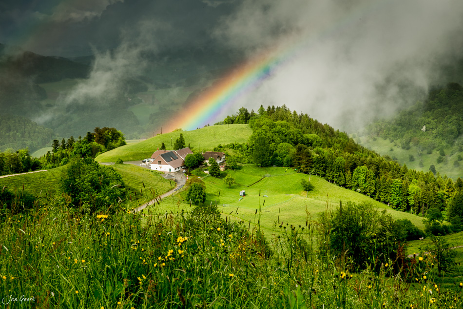 Regenbogen über grüner Berglandschaft mit Bauernhof in der Bölchenregion während Frühlingssturm Schweiz Jan Geerk Fotograf Basel