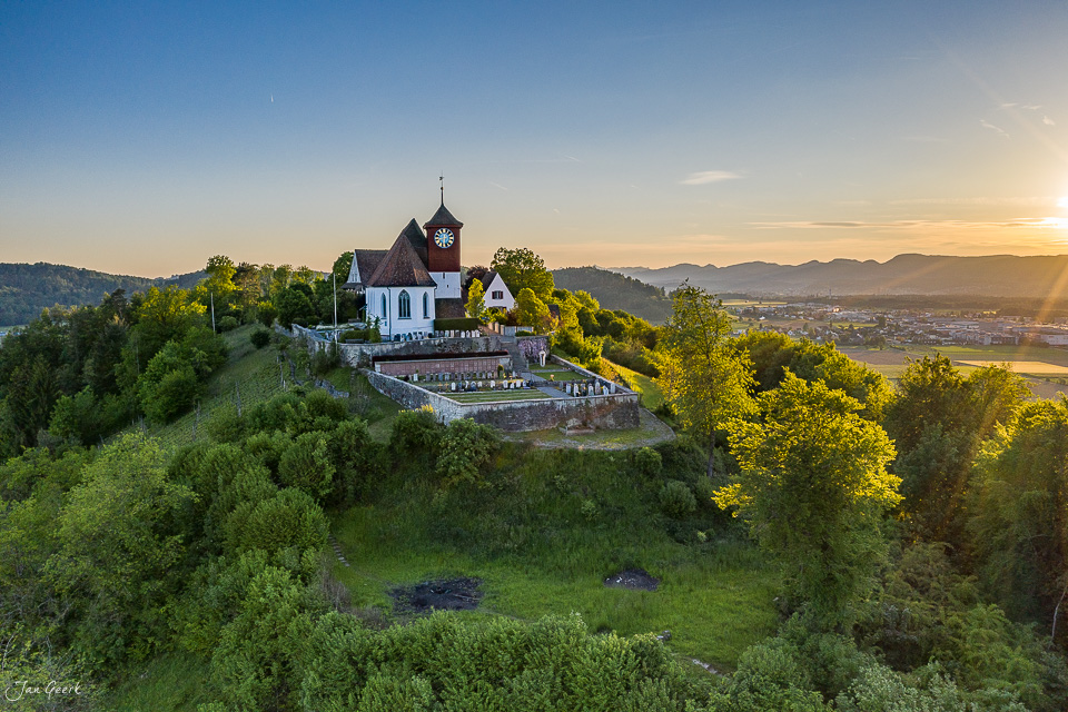 Luftaufnahme der Lenzburg Schlosskirche im Frühlingslicht mit Blick übers Aargauer Mittelland und die Jura-Hügelkette in der Schweiz – Jan Geerk Fotograf Basel
