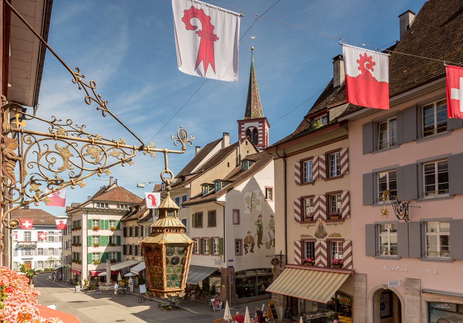 Historische Altstadt Liestal mit bunten Fachwerkhäusern, Kirche und Flaggen im Sonnenlicht, Baselland Schweiz – Jan Geerk Fotograf Basel