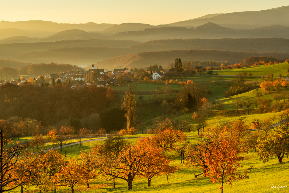 Herbstliche Landschaft bei Nuglar mit golden gefärbten Bäumen, grünen Wiesen und fernem Dorf in Baselland Schweiz – Jan Geerk Fotograf Basel