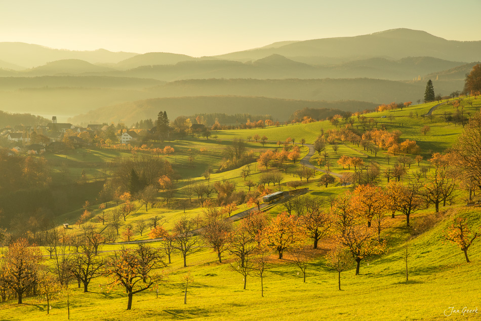 Herbstliche Hügellandschaft Nuglar mit Obstbäumen, Wiesen und Zug in goldenem Morgenlicht, Baseland Schweiz – Jan Geerk Fotograf Basel