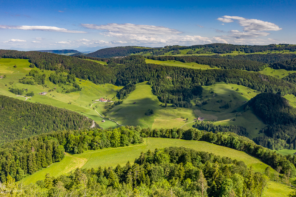 Luftaufnahme des Nunningen Tals mit grünen Wiesen, Wäldern und verstreuten Bauernhöfen an einem sonnigen Sommertag in der Schweiz – Fotograf Jan Geerk Basel