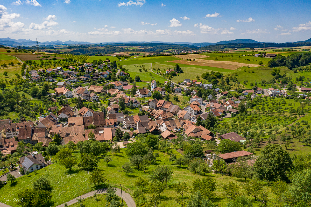 Luftaufnahme des Dorfes Oltingen im Baselbiet mit grünen Wiesen und Bauernhöfen, sonniger Sommertag, Nordwestschweiz – Jan Geerk Fotograf Basel