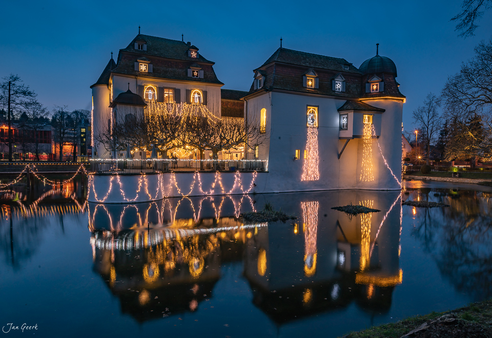 Schloss Bottmingen festlich illuminiert bei Dämmerung mit Weihnachtsbeleuchtung und Spiegelung im Wasser, Baselland Schweiz Jan Geerk Fotograf Basel