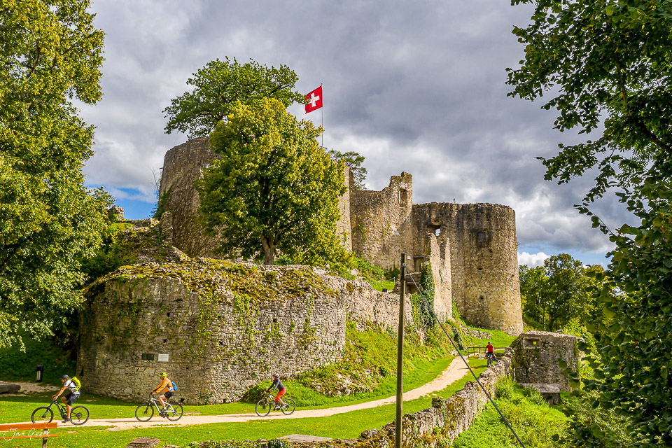 Schloss Dorneck mit Schweizer Flagge, Radfahrer auf grüner Wiese, sommerliche Lichtstimmung, Solothurn-Dornach Schweiz – Jan Geerk Fotograf Basel