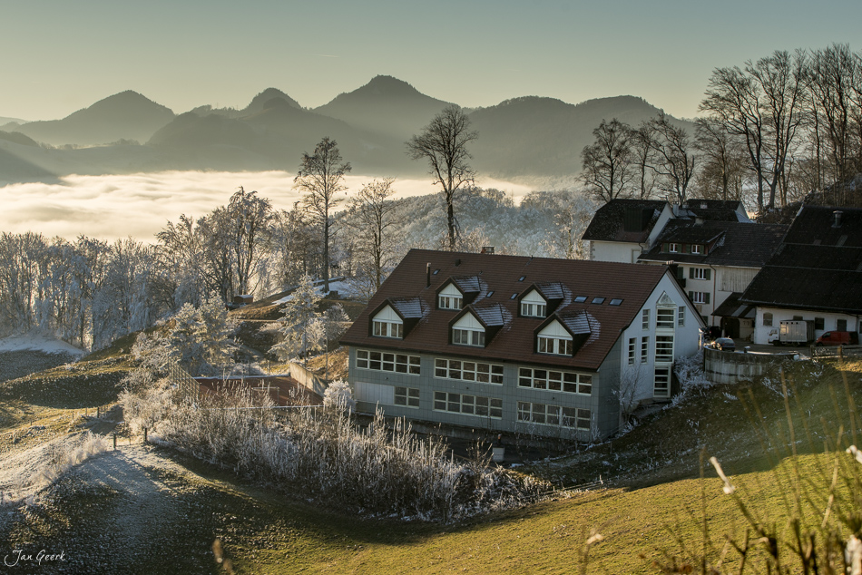 Winterlandschaft Wisen mit Nebelwelle, schneebedeckte Häuser und Berge im Hintergrund, Baselland Schweiz – Jan Geerk Fotograf Basel