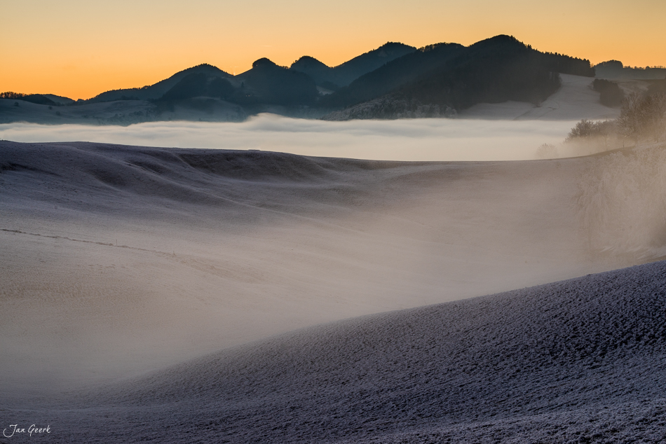 Nebelwelle über Wisen mit Bergsilhouetten bei Sonnenaufgang im Winter, Baselland Schweiz – Jan Geerk Fotograf Basel