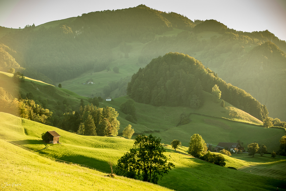 Grüne Hügellandschaft am Passwang mit traditionellem Bauernhaus, golden beleuchtete Herbststimmung, Jura Nordwestschweiz – Jan Geerk Fotograf Basel