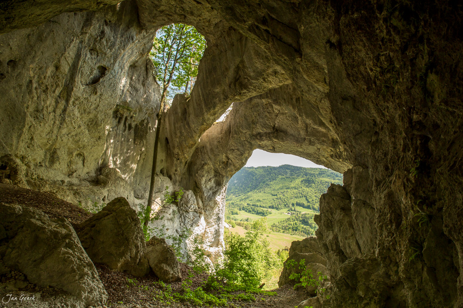 Höhlenöffnung in der Wolfsschlucht Welschenrohr mit Blick auf grüne Juralandschaft im Frühling, Schweiz – Jan Geerk Fotograf Basel