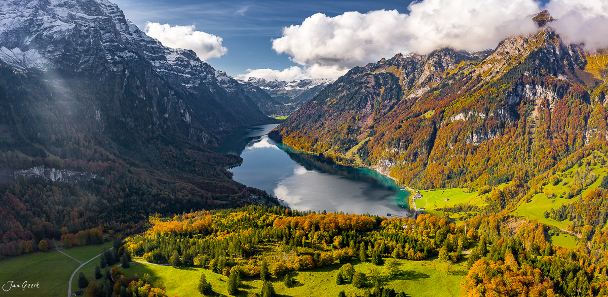 Luftaufnahme des Klöntalersees mit herbstlich gefärbten Wäldern, schneebedeckten Berggipfeln und türkisem Wasser in der Schweiz – Jan Geerk Fotograf Basel