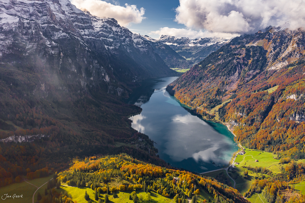 Luftaufnahme Klöntalersee mit herbstlich gefärbten Wäldern, Schnee-Alpen im Hintergrund, Herbstlicht, Zentralschweiz – Jan Geerk Fotograf Basel